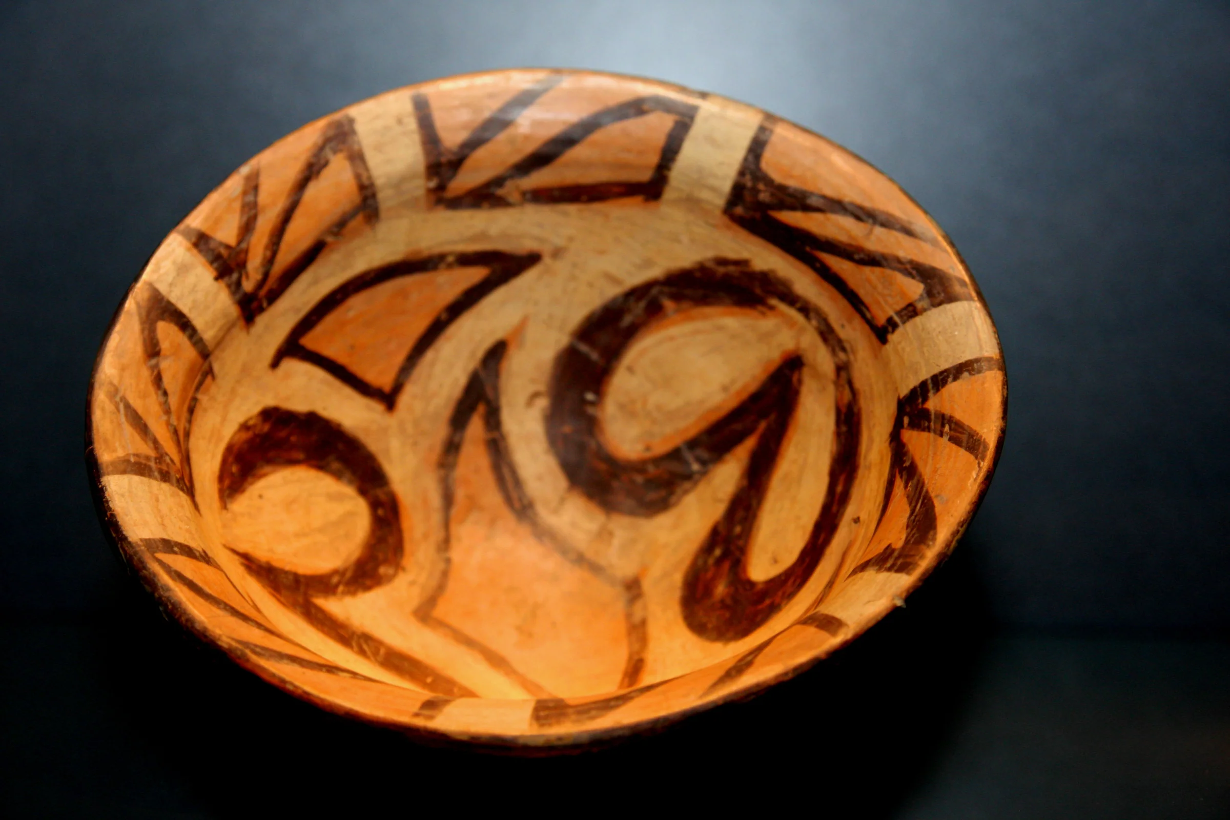 A painted ceramic bowl with black spirals on an orange ground
