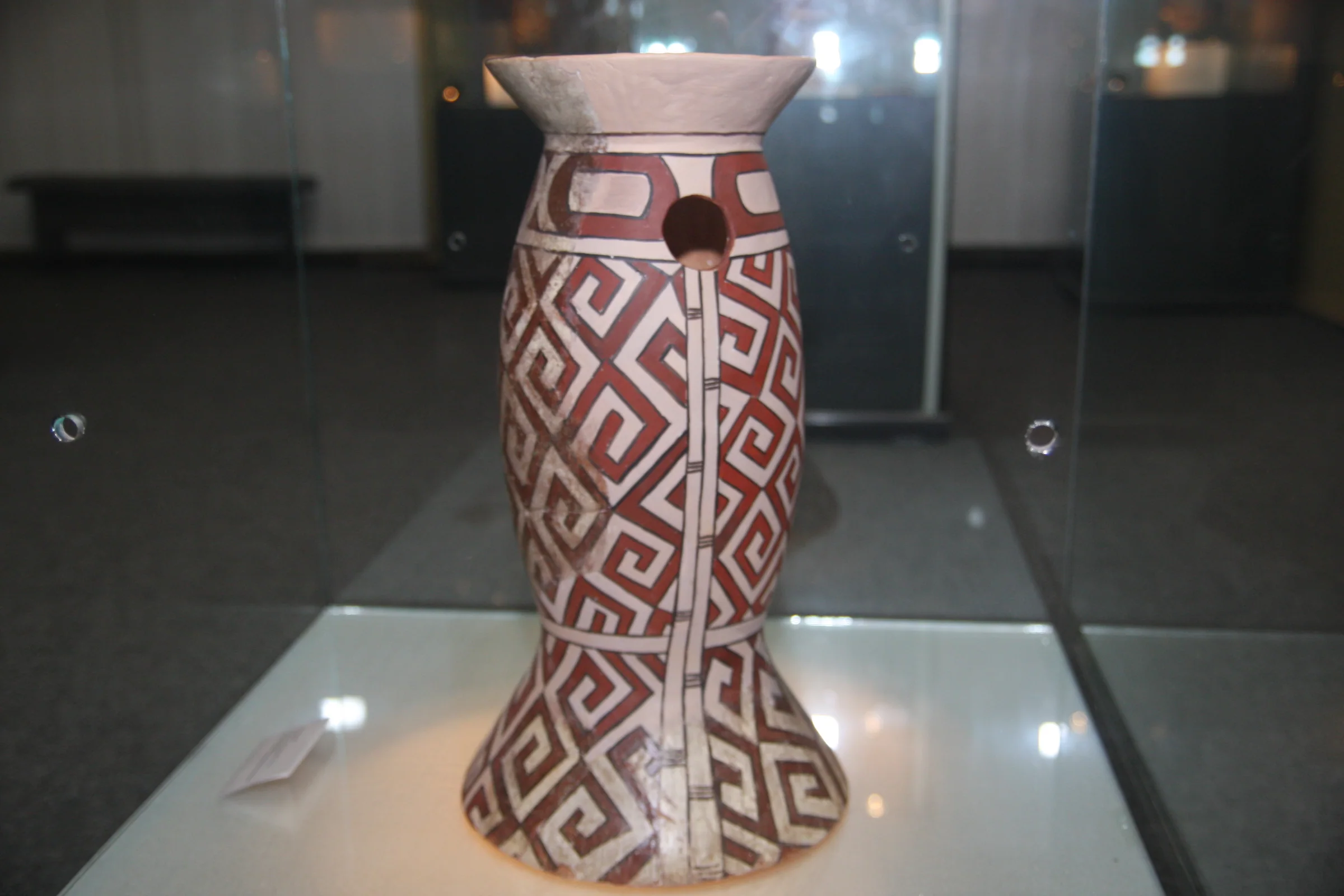 A ceramic vessel with a red geometric pattern on a white ground, in a display case