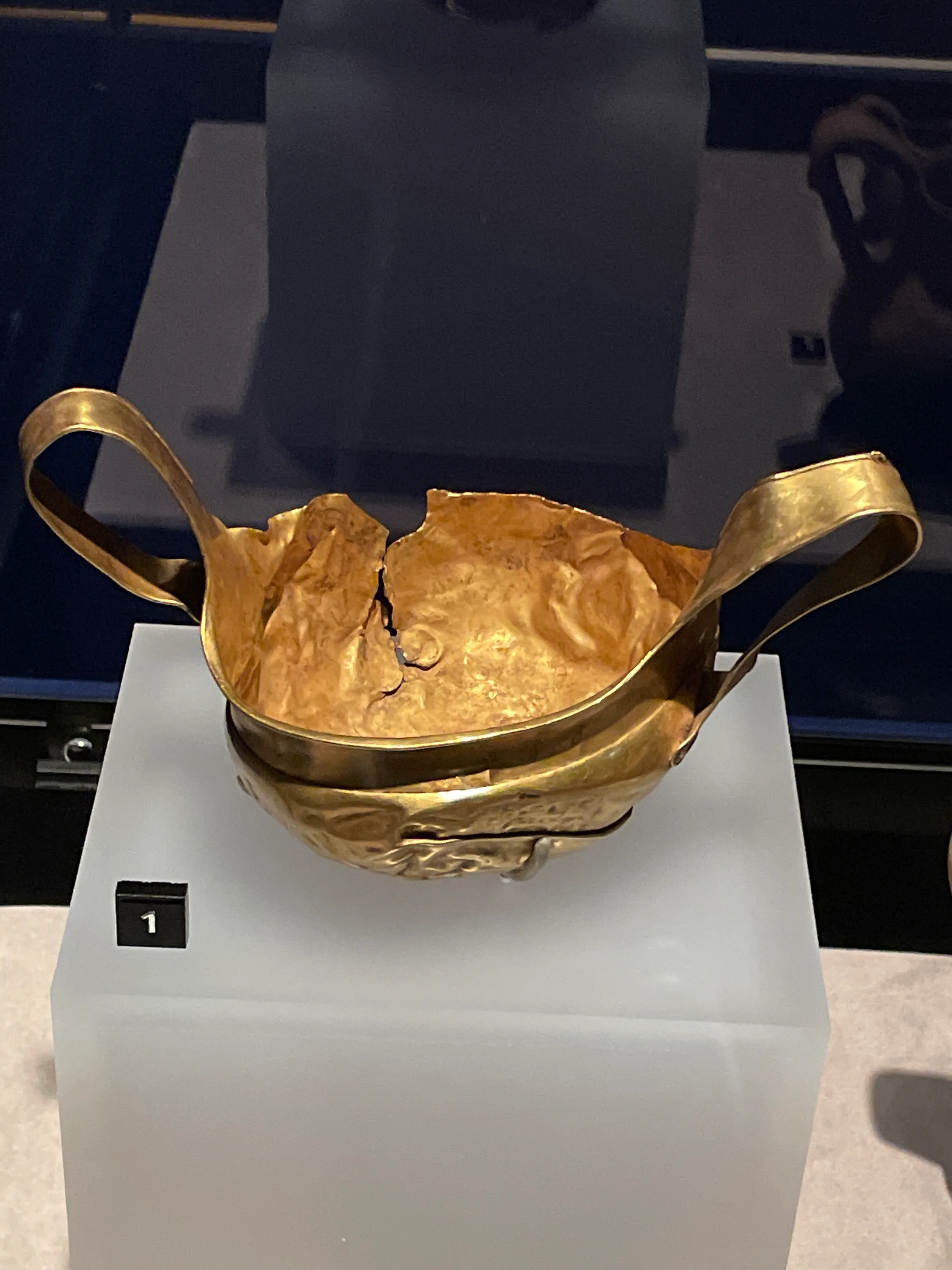 A two-handled gold cup on a white plinth